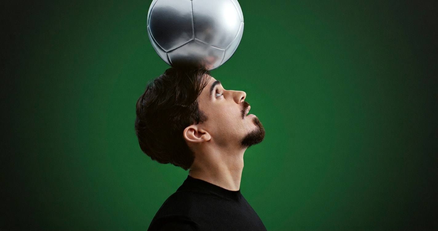 Modelo com bola de futebol na cabeça em fundo verde escuro.