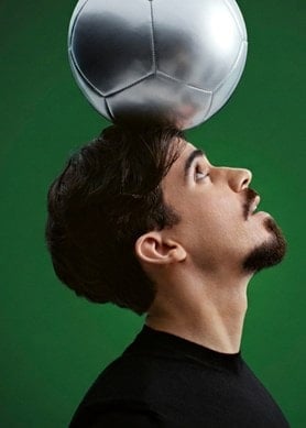 Modelo com bola de futebol na cabeça em fundo verde escuro.